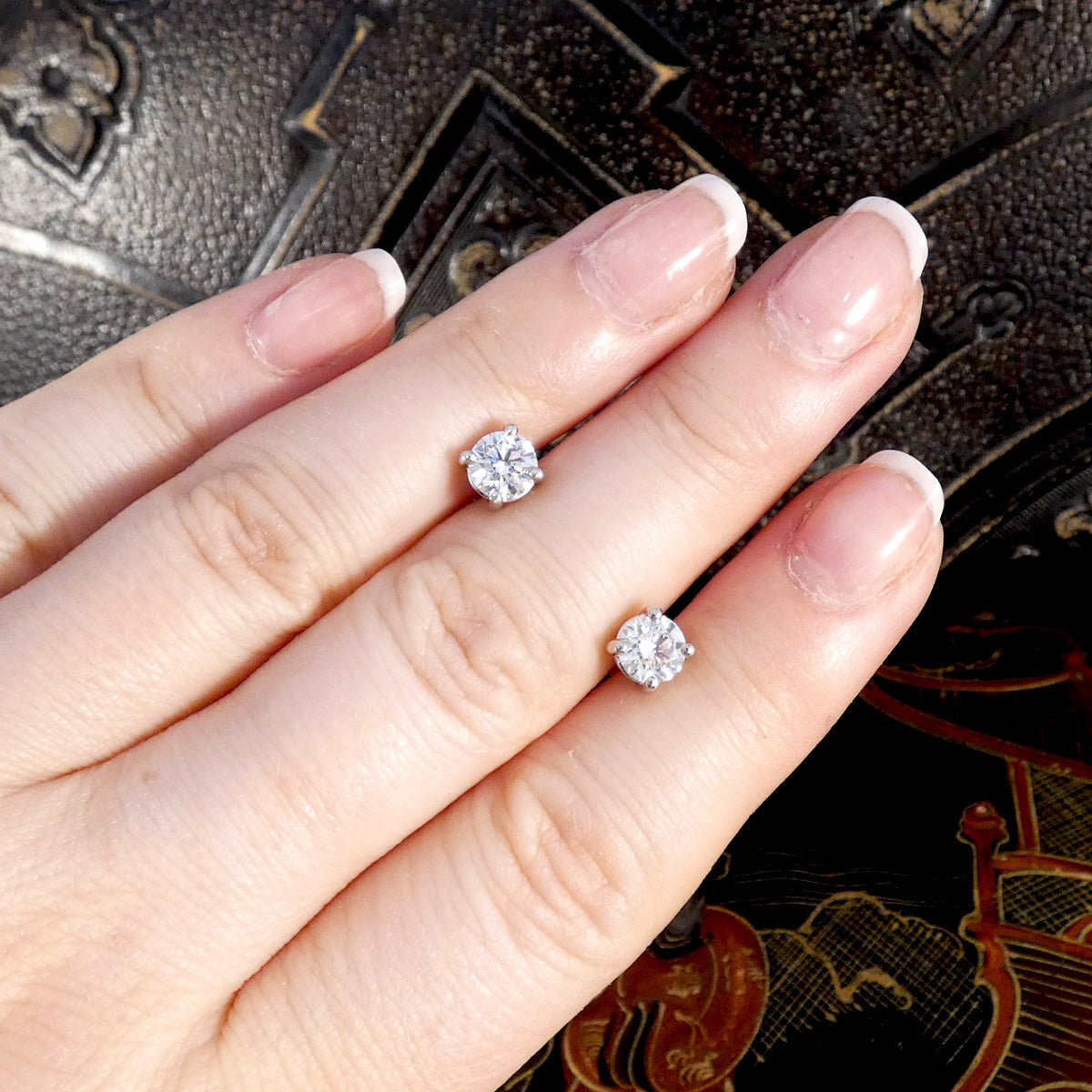Diamond and Platinum stud earrings on a hand with a decorative background.