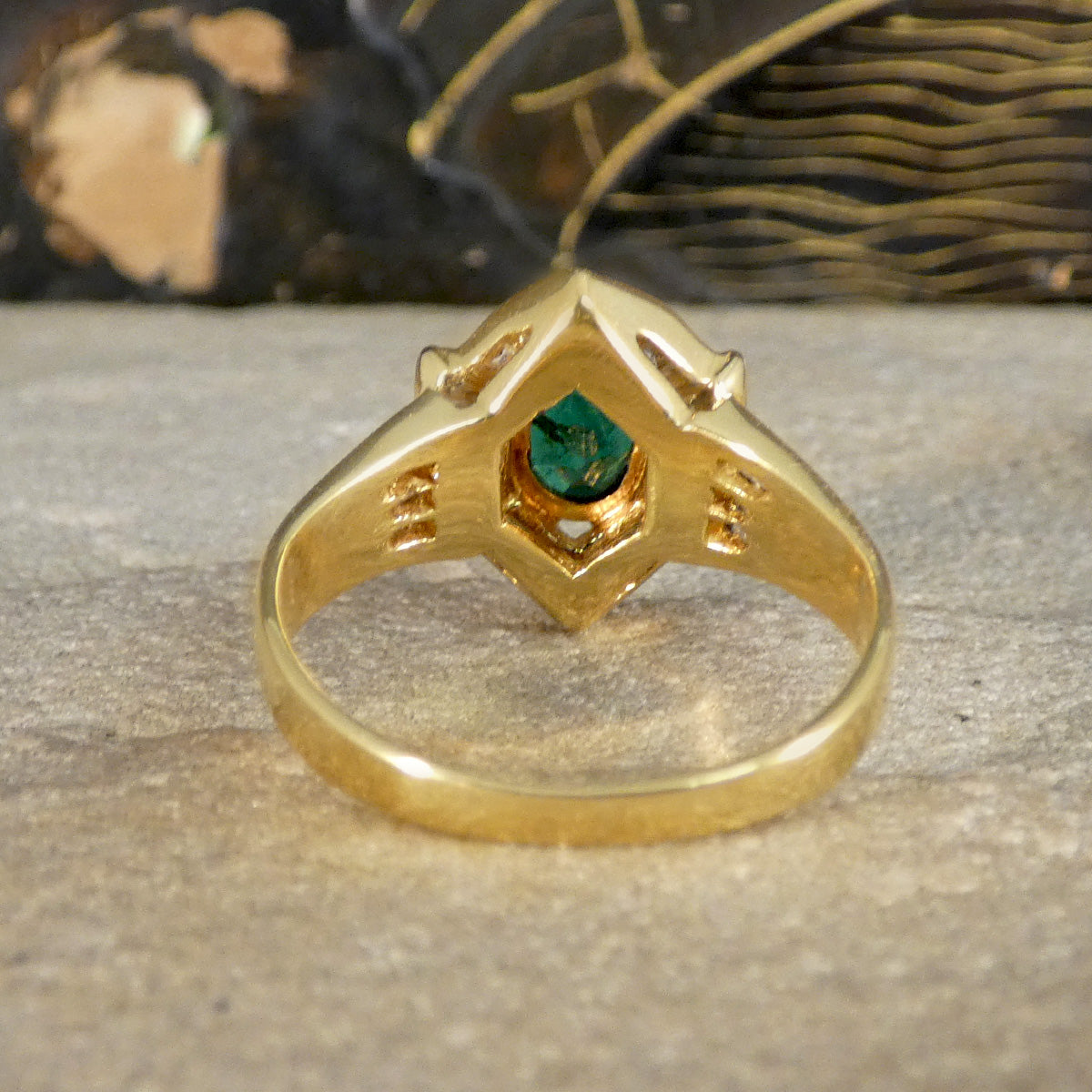 Rear view of an emerald and tapered diamond cluster ring in 18ct yellow gold, showing the openwork gallery and secure bezel setting that highlights the vivid green emerald cent stone.e
