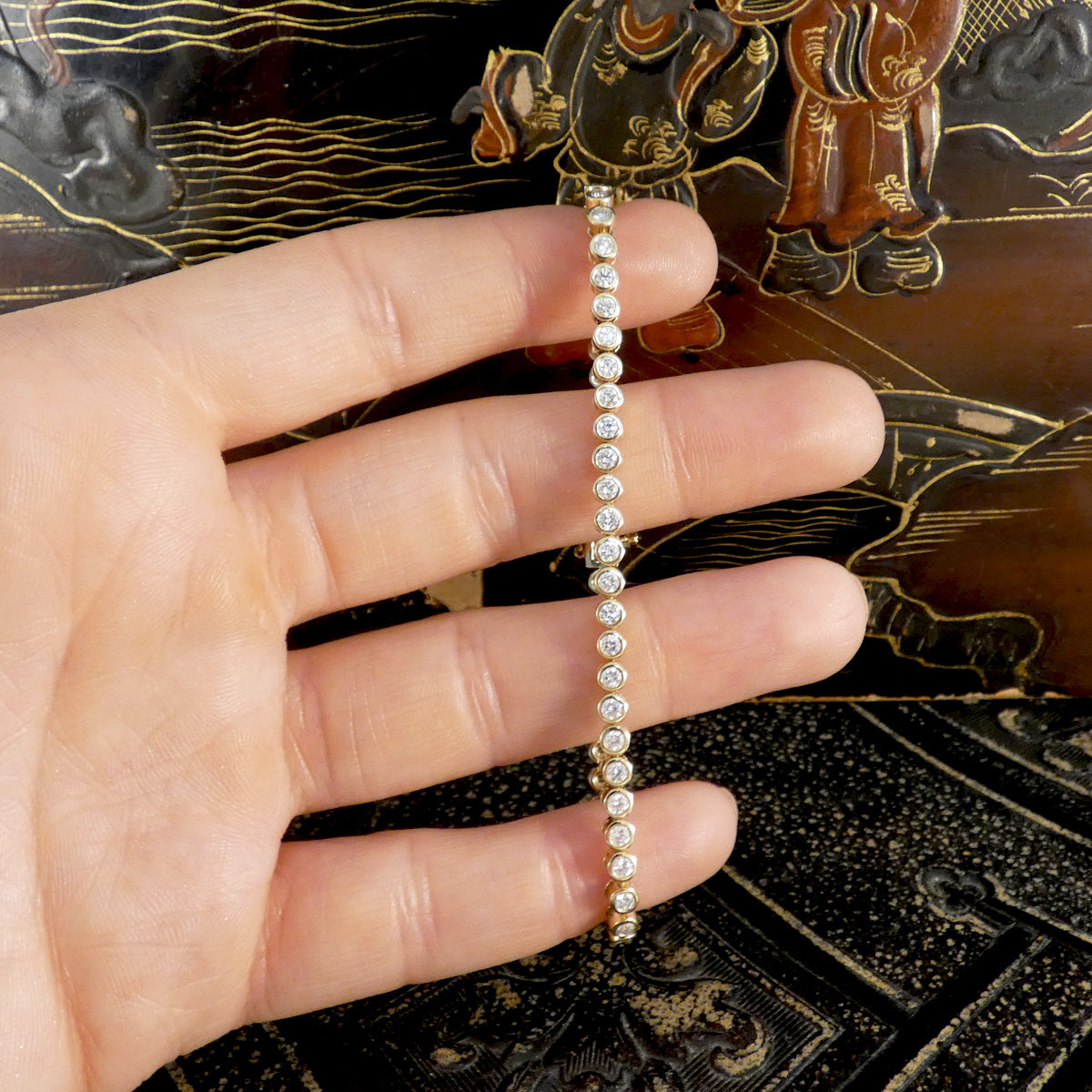 Gold tennis bracelet with diamond in full gold bezel rub over settings held on the hand to see size ratio.