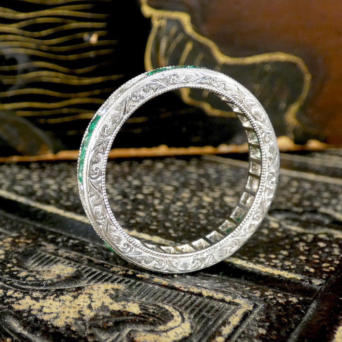 Side profile of Platinum engraved ring. Set with Emeralds and diamonds round the full band with detail set into the gallery all the way around the band.