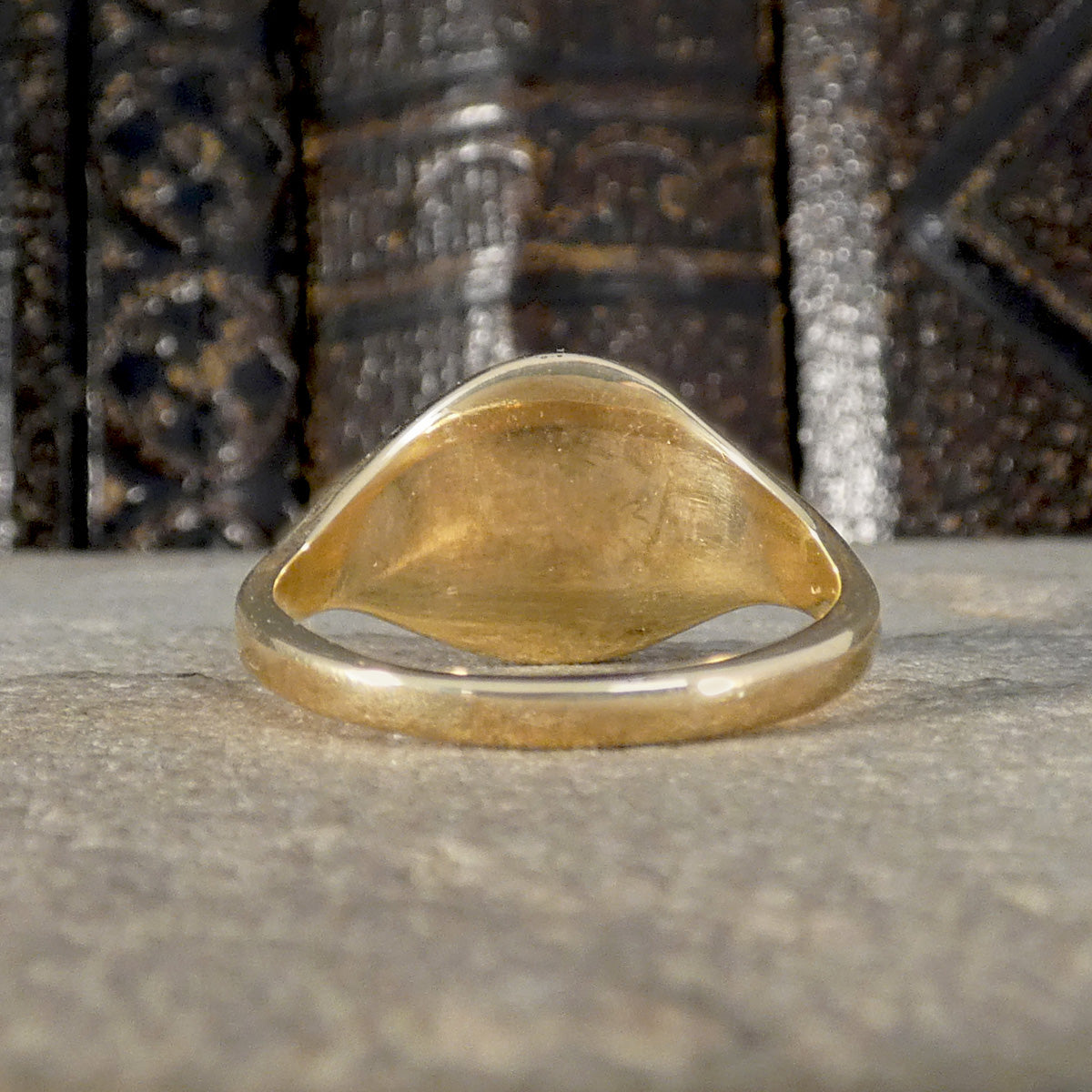 The back of a Gold signet ring on a textured surface with a metallic background