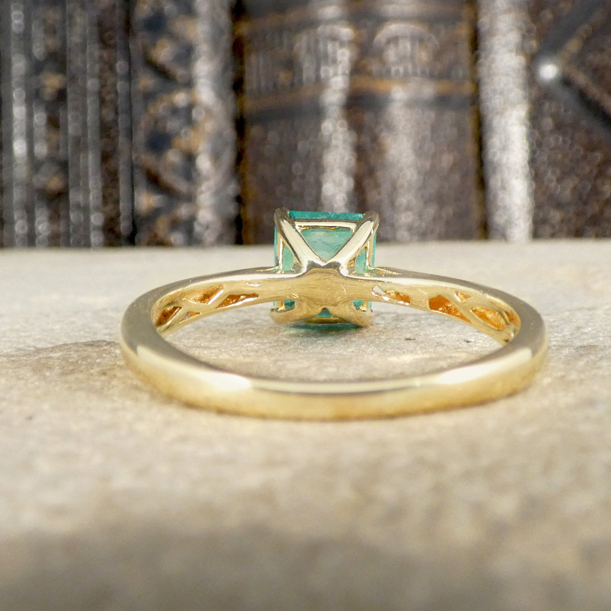 Gold ring with a green gemstone on a textured surface shown from the back with hollowed shank.