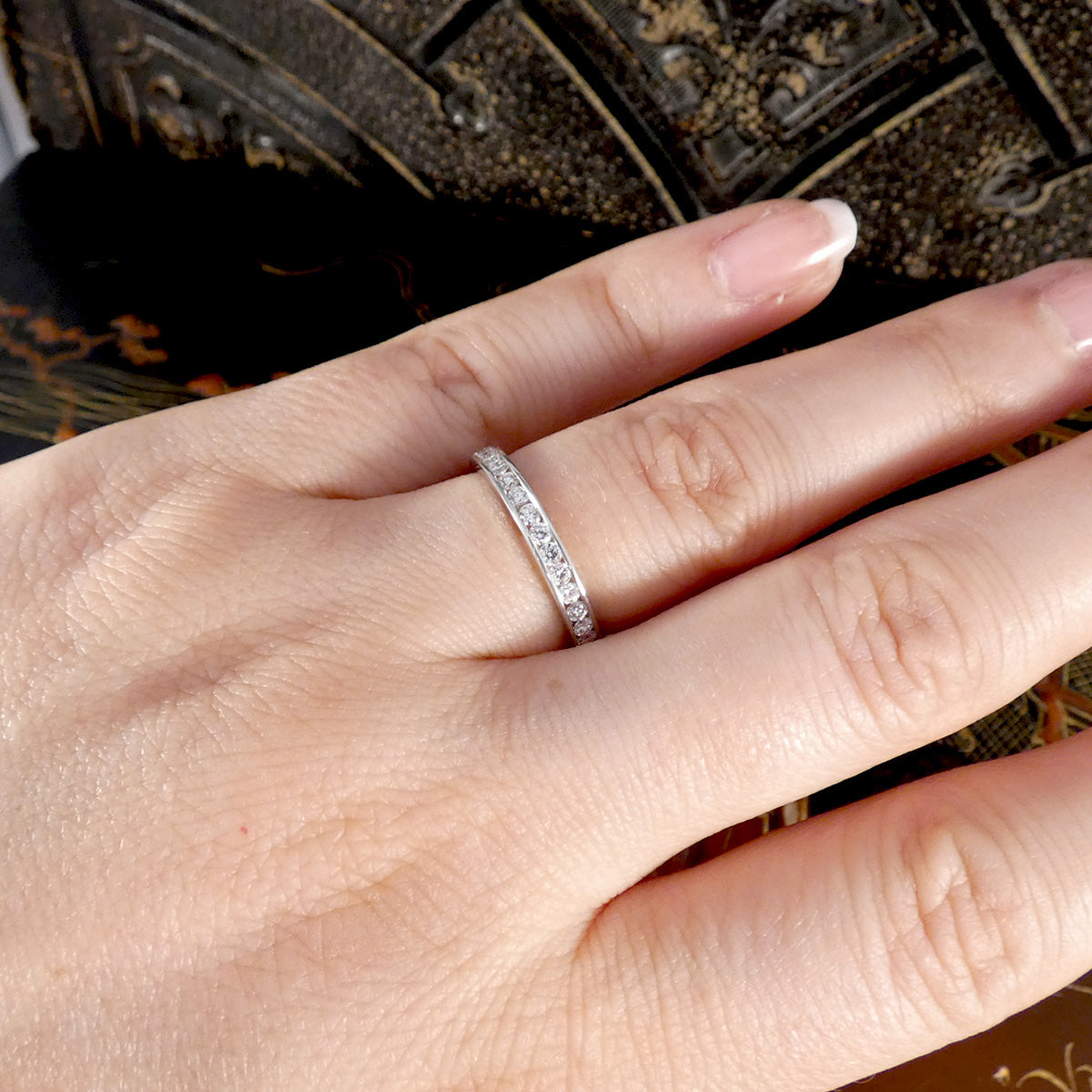 Hand wearing a platinum ring with Diamonds set against a dark textured background