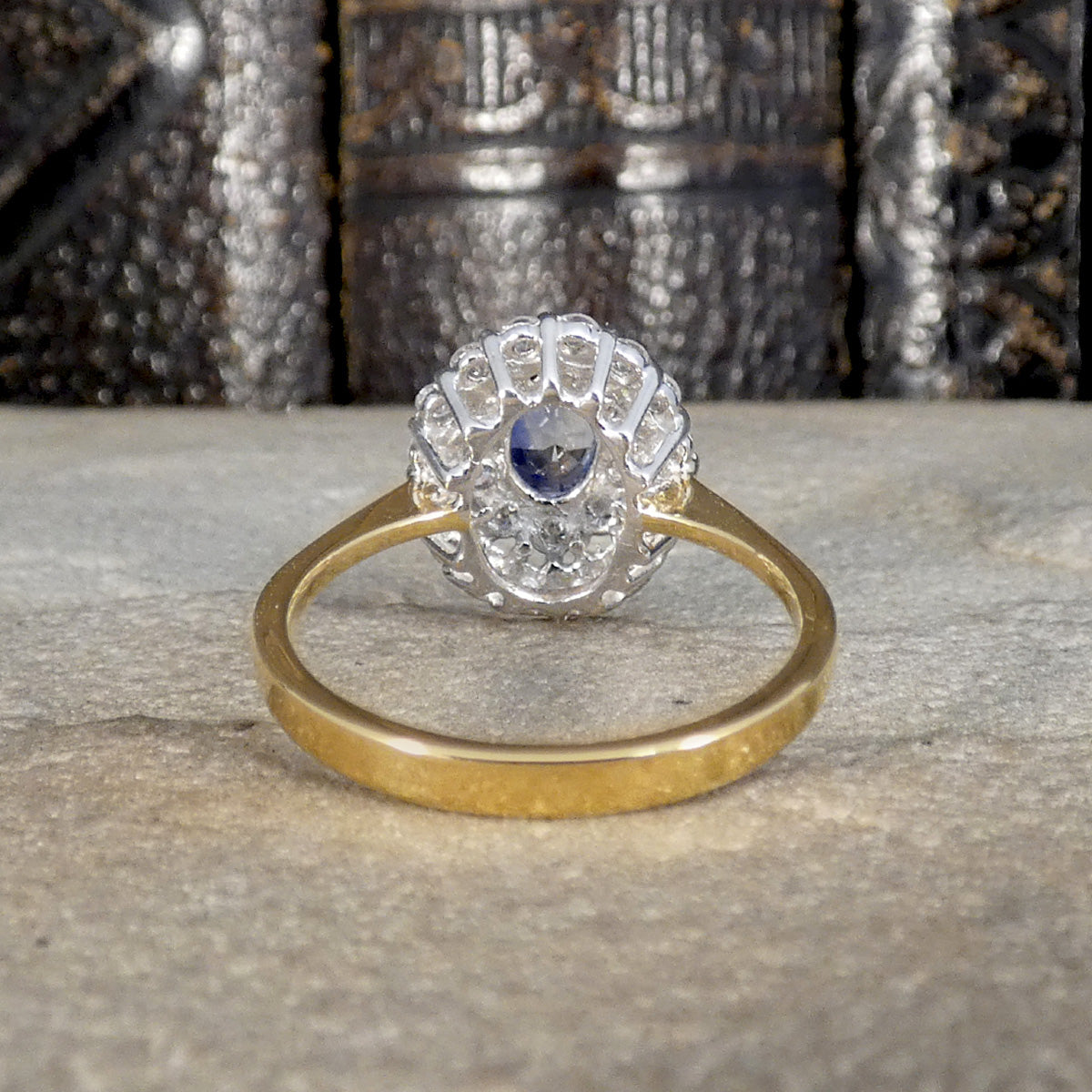 Back view of Vintage-style cluster ring featuring a central oval blue sapphire surrounded by multiple round brilliant-cut diamonds, set in white and yellow gold.