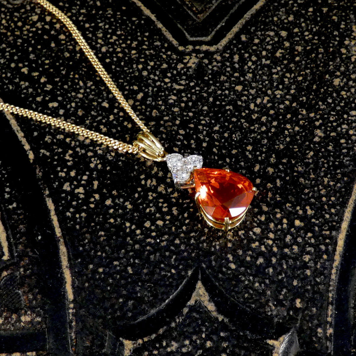 Jewellery with a pear-shaped red gemstone and diamond pendant on a gold chain against a black textured background.