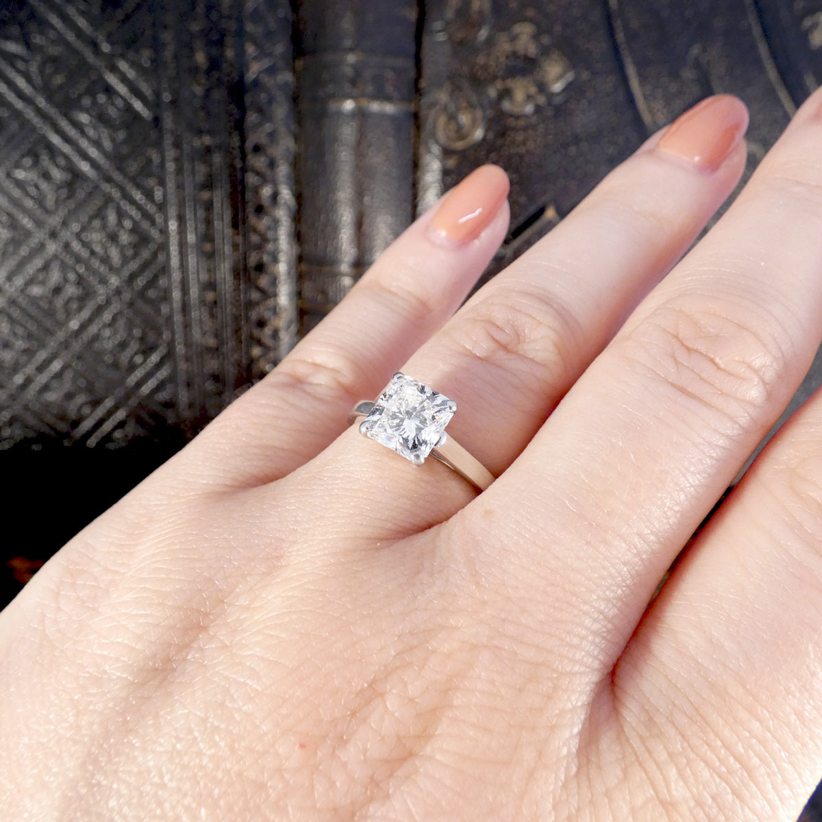 Diamond ring on a hand with a textured fabric background showing the size and shape reference.