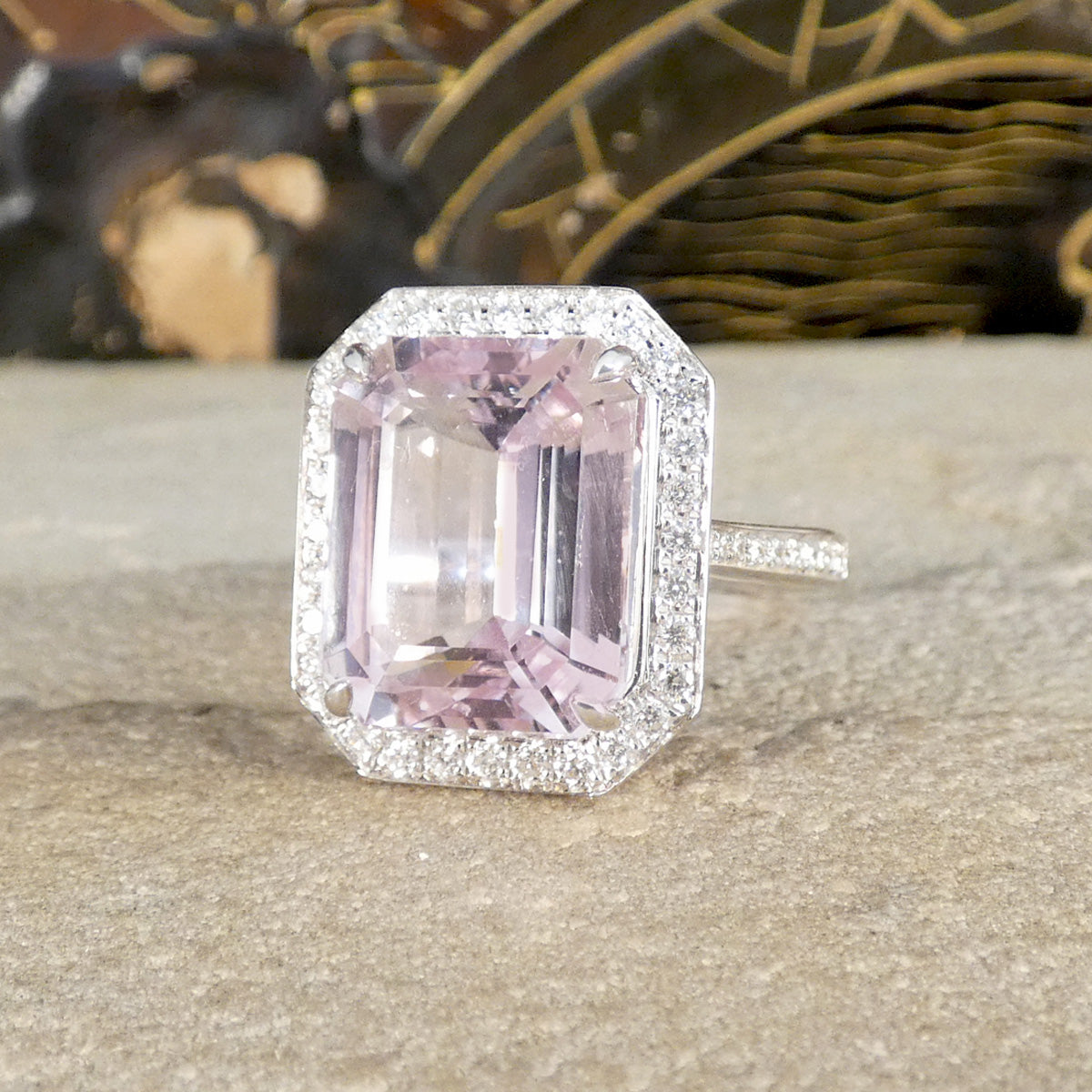 Pink gemstone ring with diamond accents on a textured surface