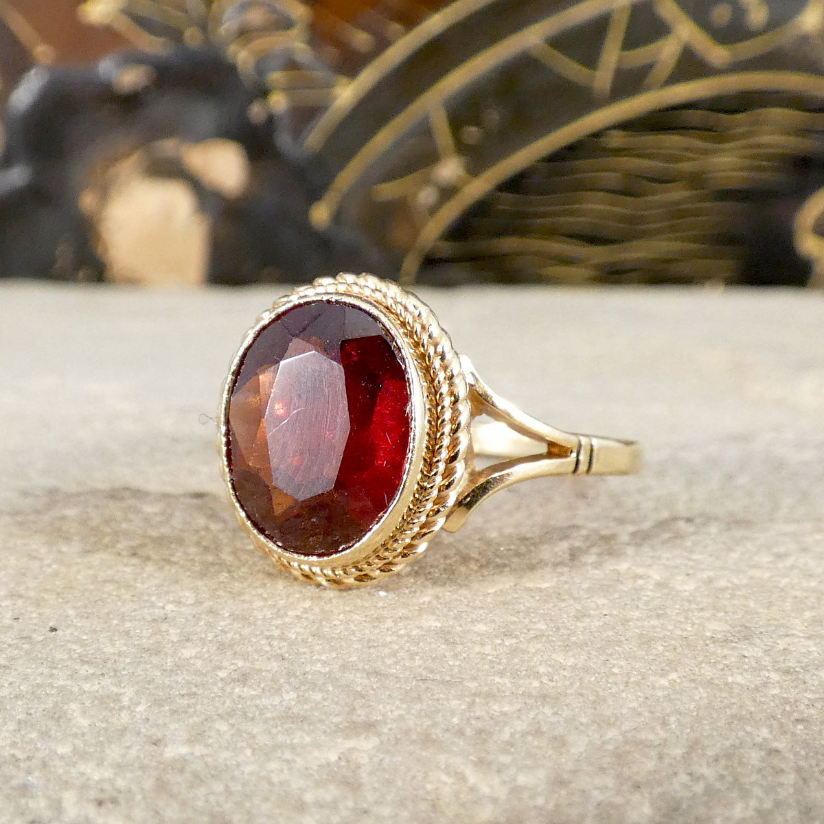 Gold ring with a red garnet single gemstone on a textured surface