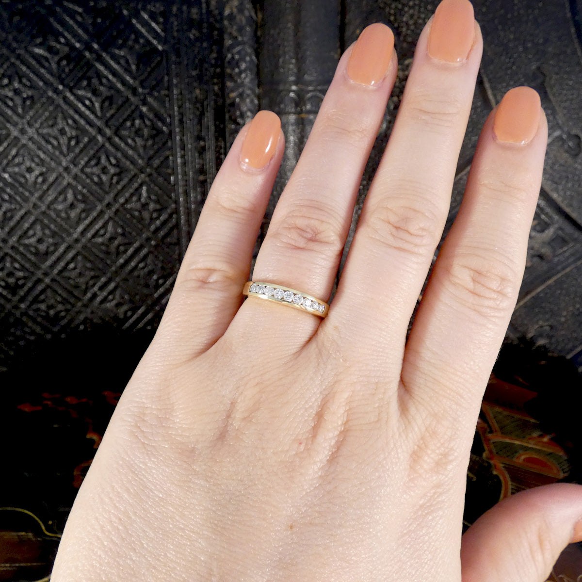Hand wearing a gold ring with a textured black background. Showing ring size and shape reference.
