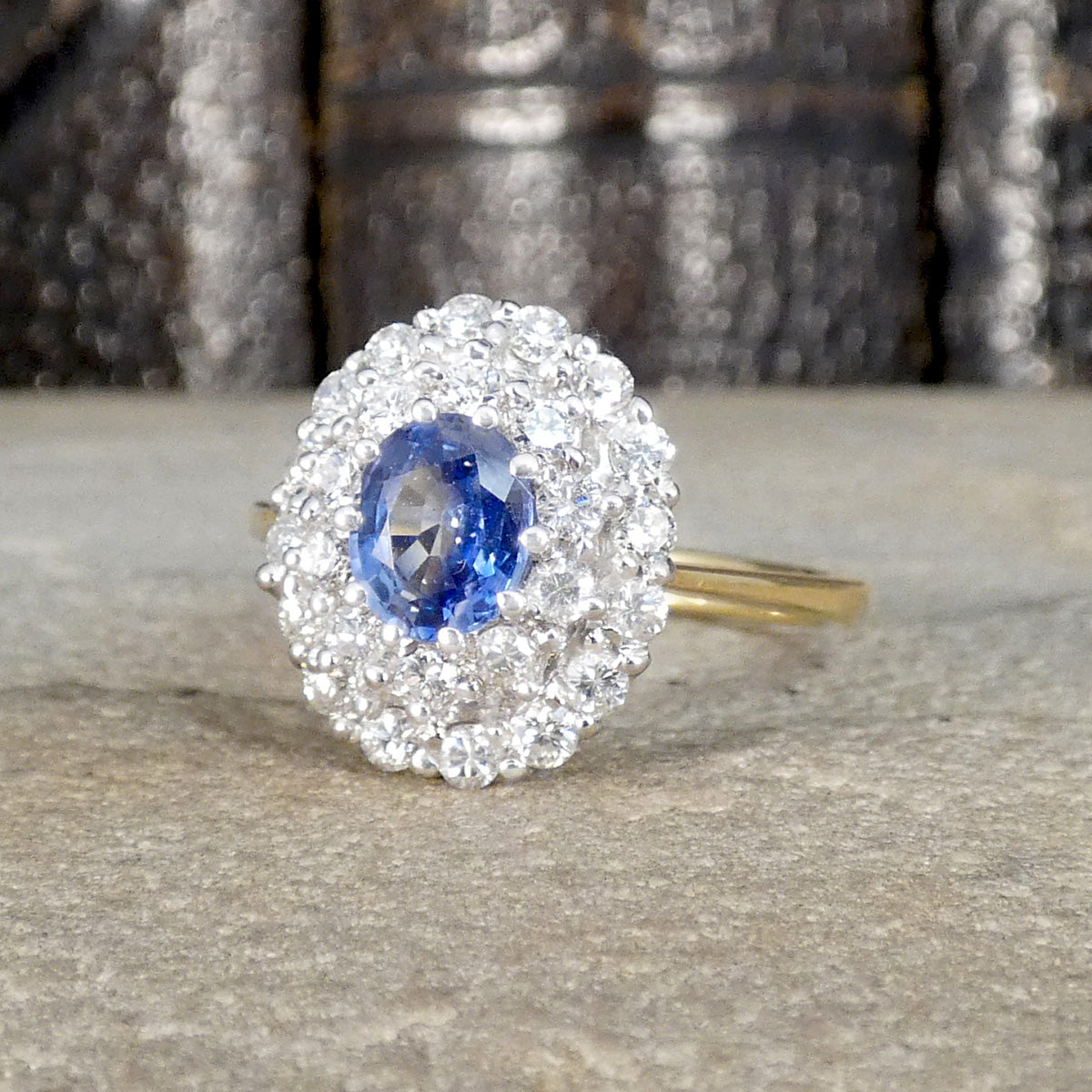 Vintage-style cluster ring featuring a central oval blue sapphire surrounded by multiple round brilliant-cut diamonds, set in white and yellow gold.
