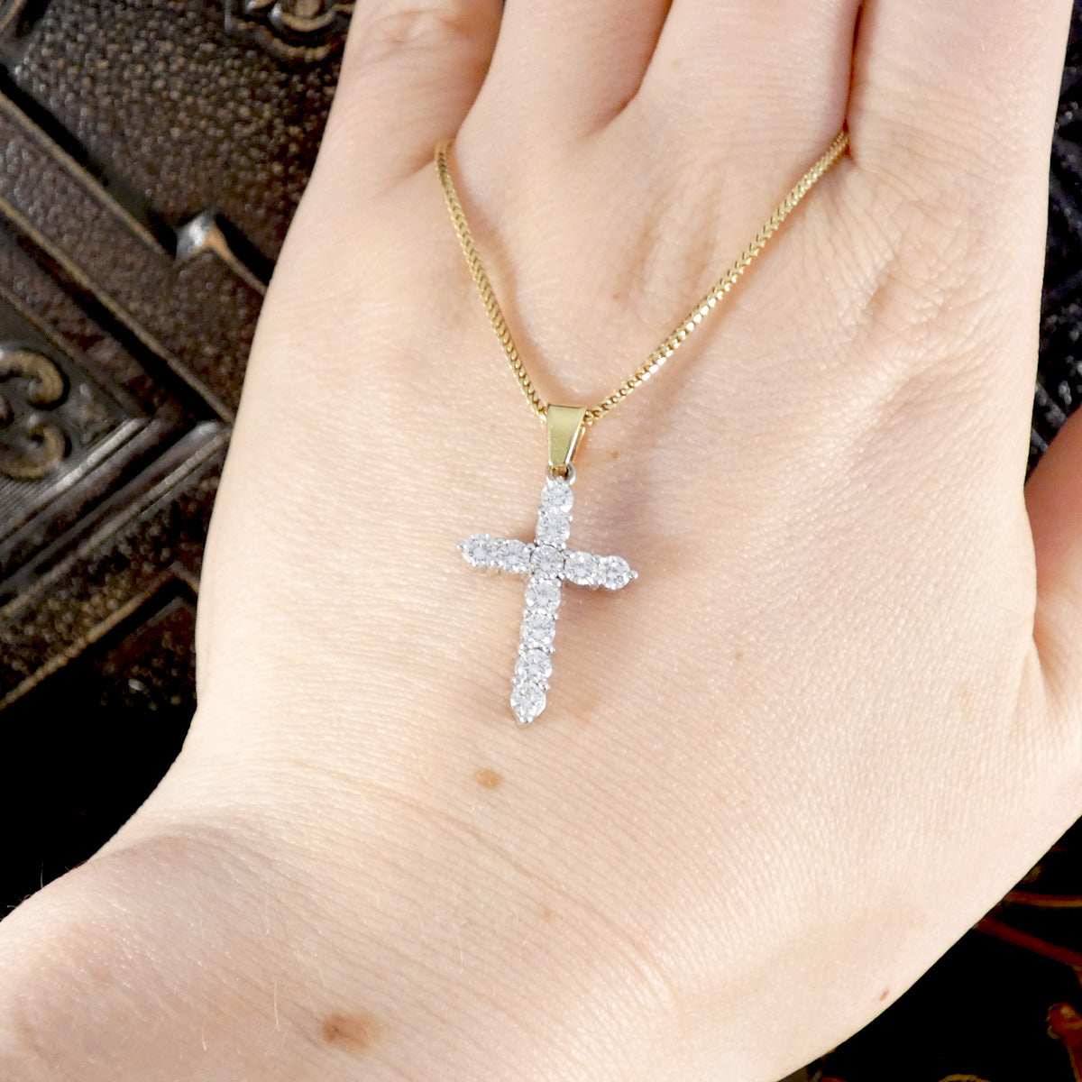 Diamond cross pendant necklace in 18ct yellow and white gold, shown worn on a hand to display its elegant size and sparkle.