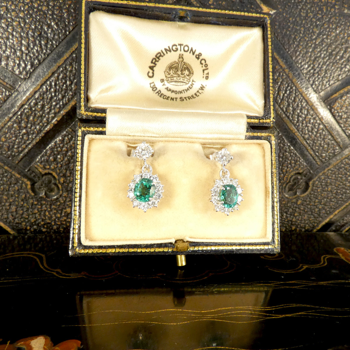 A beautiful pair of Oval Cut Emeralds surrounded by a halo of bright and sparkly diamonds hanging from a diamond stud as a drop earrings. Displayed in a vintage box.
