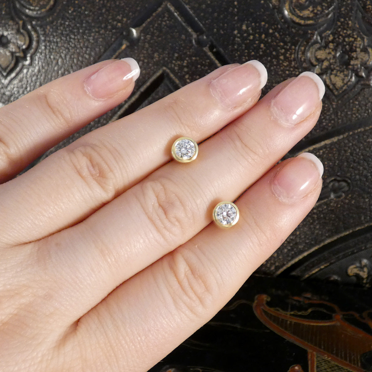 Gold earrings with diamonds on a hand against a dark textured background. Diamonds are GIA certified as G in colour and VS2 in clarity.