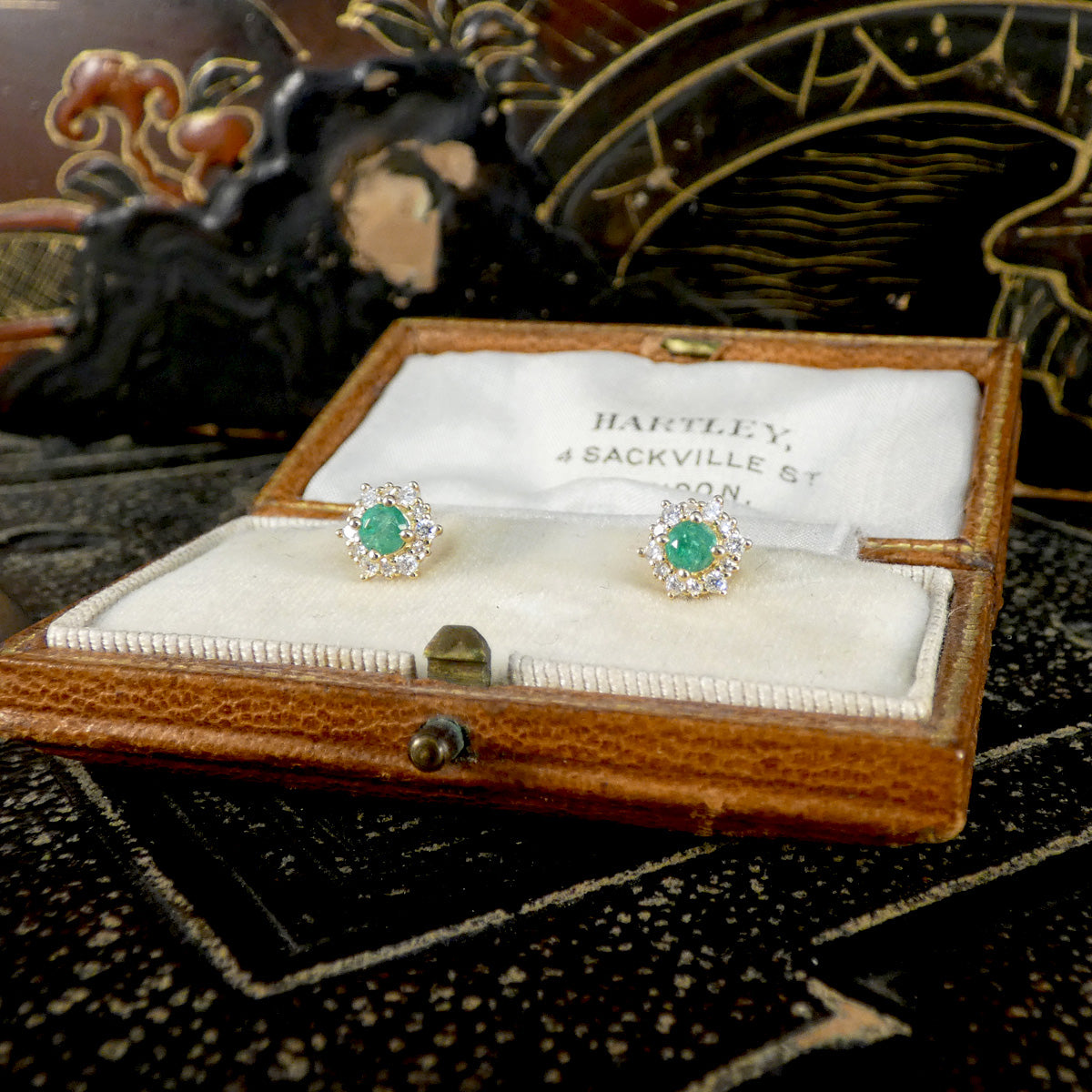 Pair of emerald and diamond earrings in a wooden box with 'Hartley' branding.