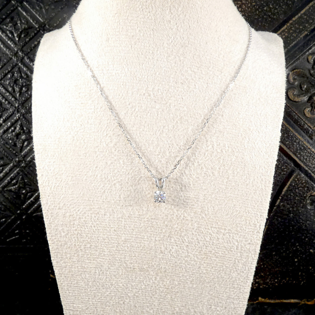 White gold necklace with a pendant on a mannequin bust against a dark textured background