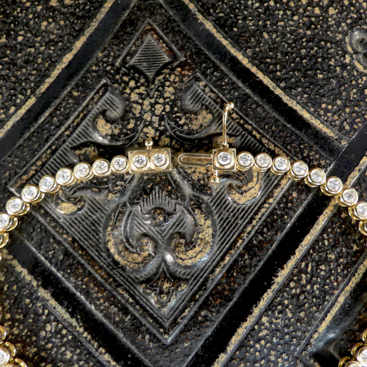 Gold bracelet with diamonds showing clasp on a textured black background