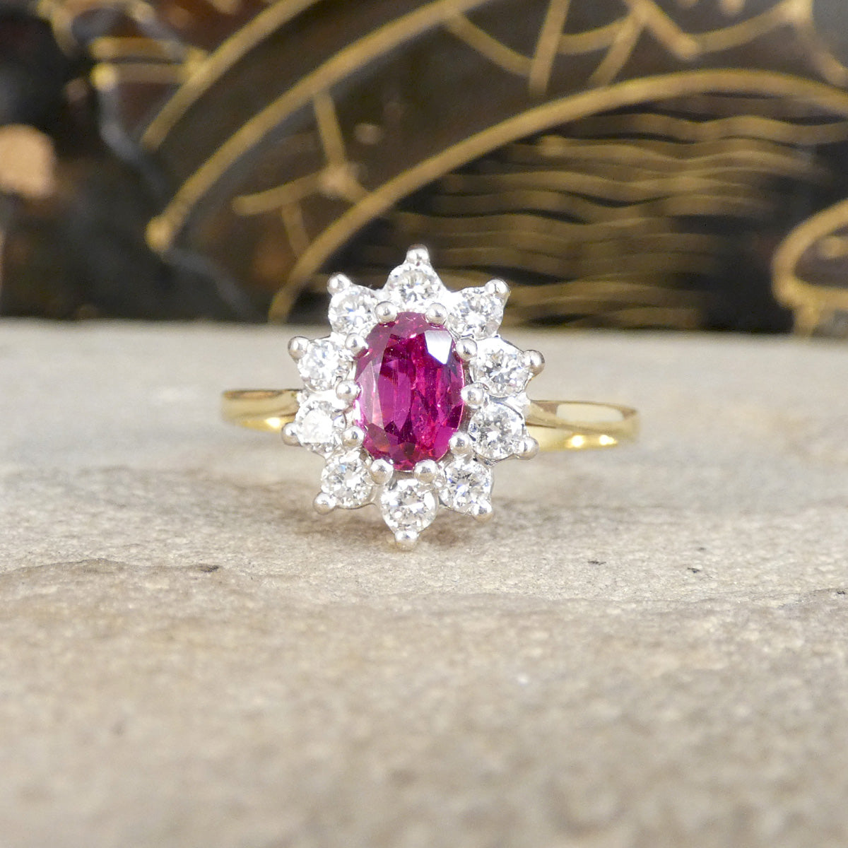 Gold ring with a pink gemstone and diamond-like stones on a textured surface.