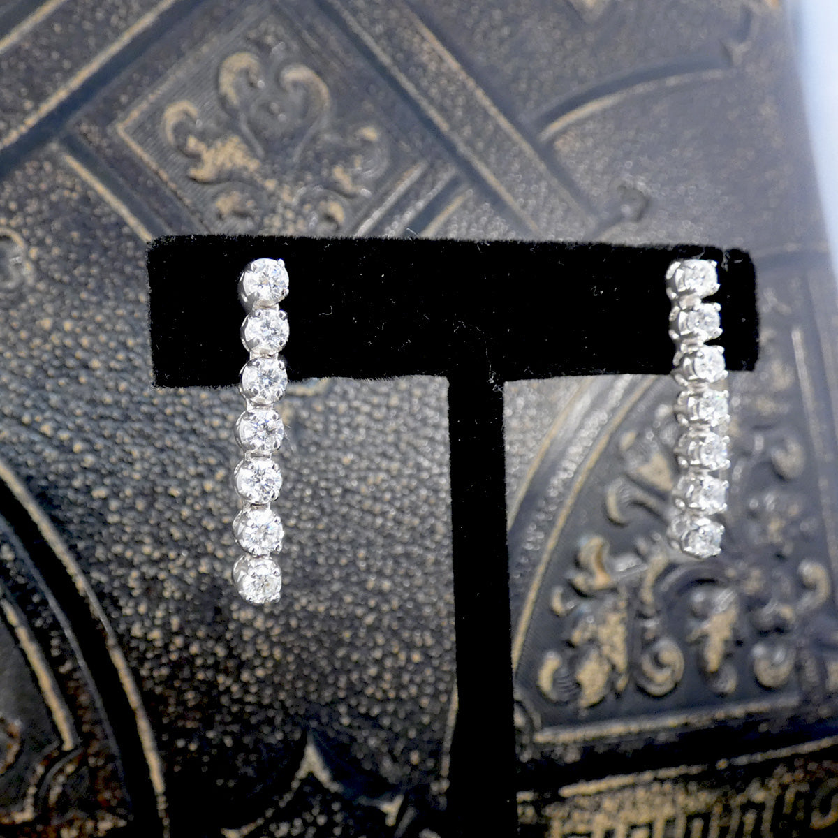 Diamond earrings on a black 'T' stand against an ornate background