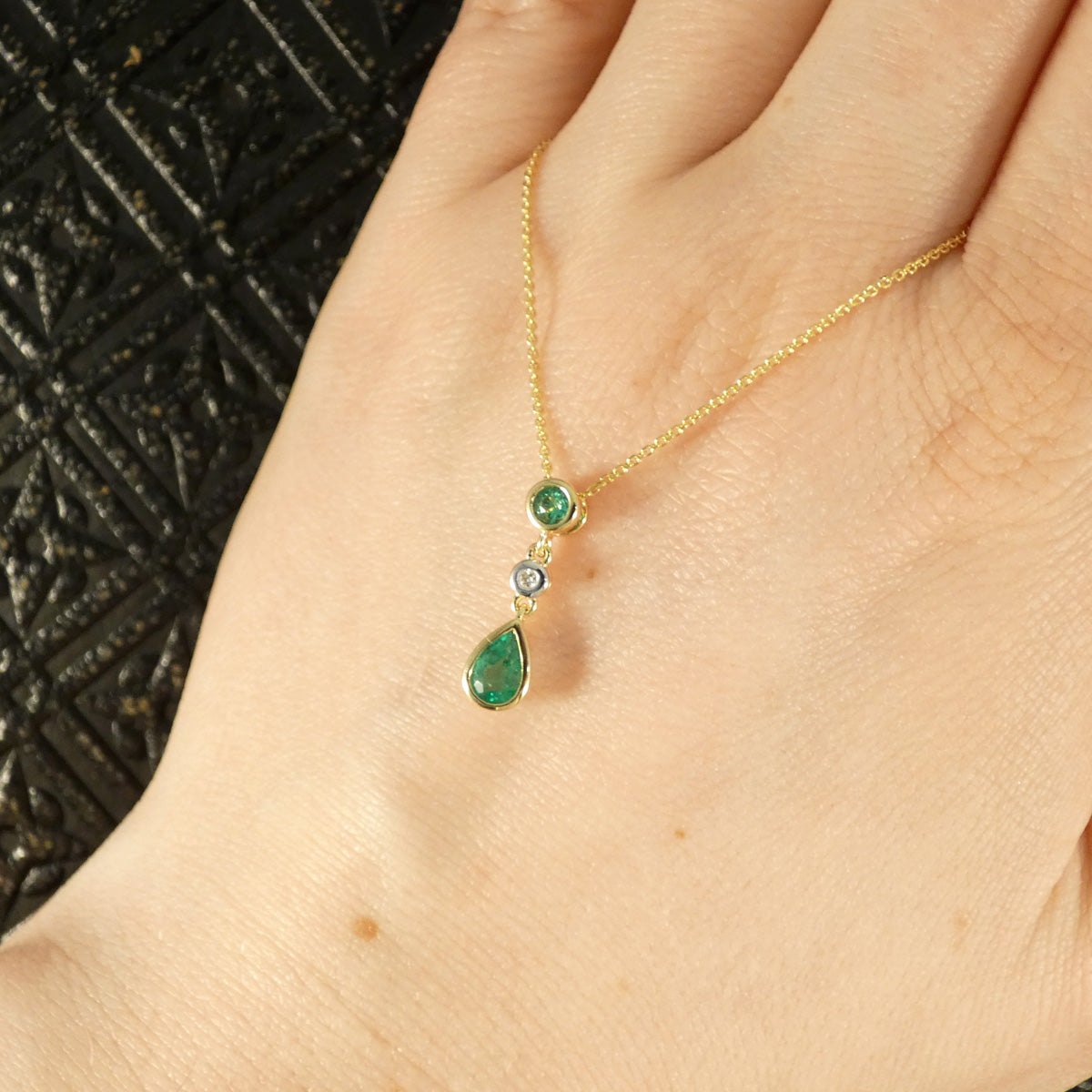 Modern Emerald and Diamond Bezel Set Drop Pendant Necklace in Yellow Gold shown on hand to see size and shape reference.
