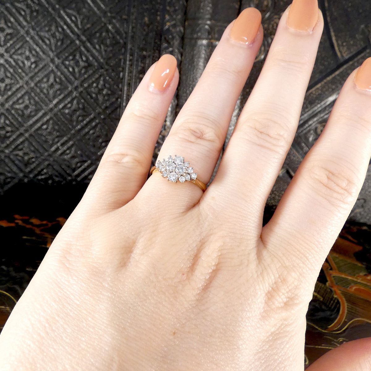 Hand wearing a diamond cluster ring with a patterned background