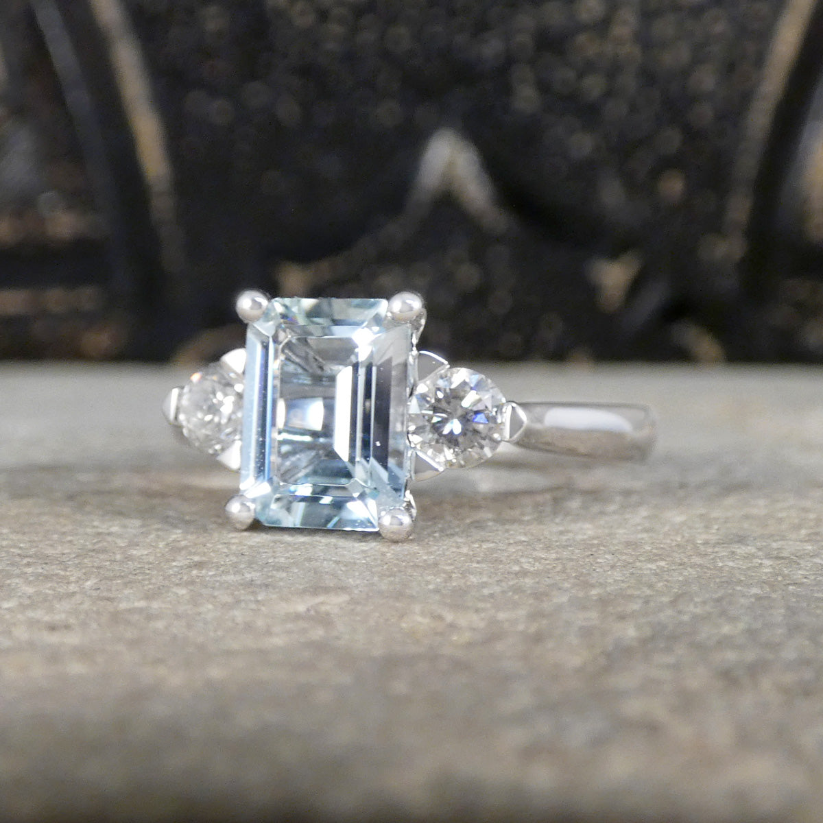Modern Emerald Cut Aquamarine and 0.35ct Diamond Three Stone Ring in Platinum. The Diamonds are set in a triangle setting giving the illusion of trillion cut diamonds.