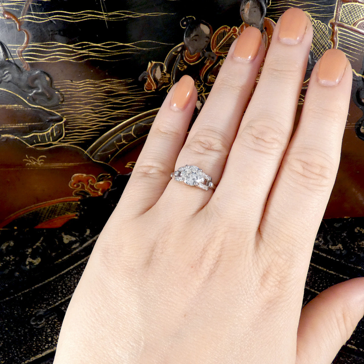 Hand wearing a diamond ring with an ornate background
