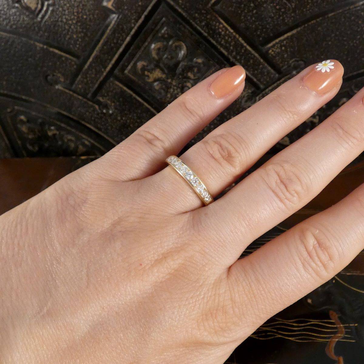 Hand wearing a gold ring with diamonds on a dark textured background