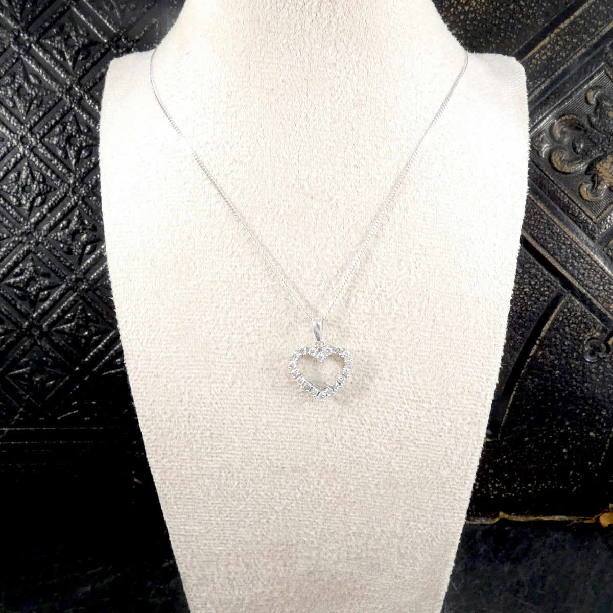 white gold necklace with a heart-shaped pendant on a mannequin against a black textured background