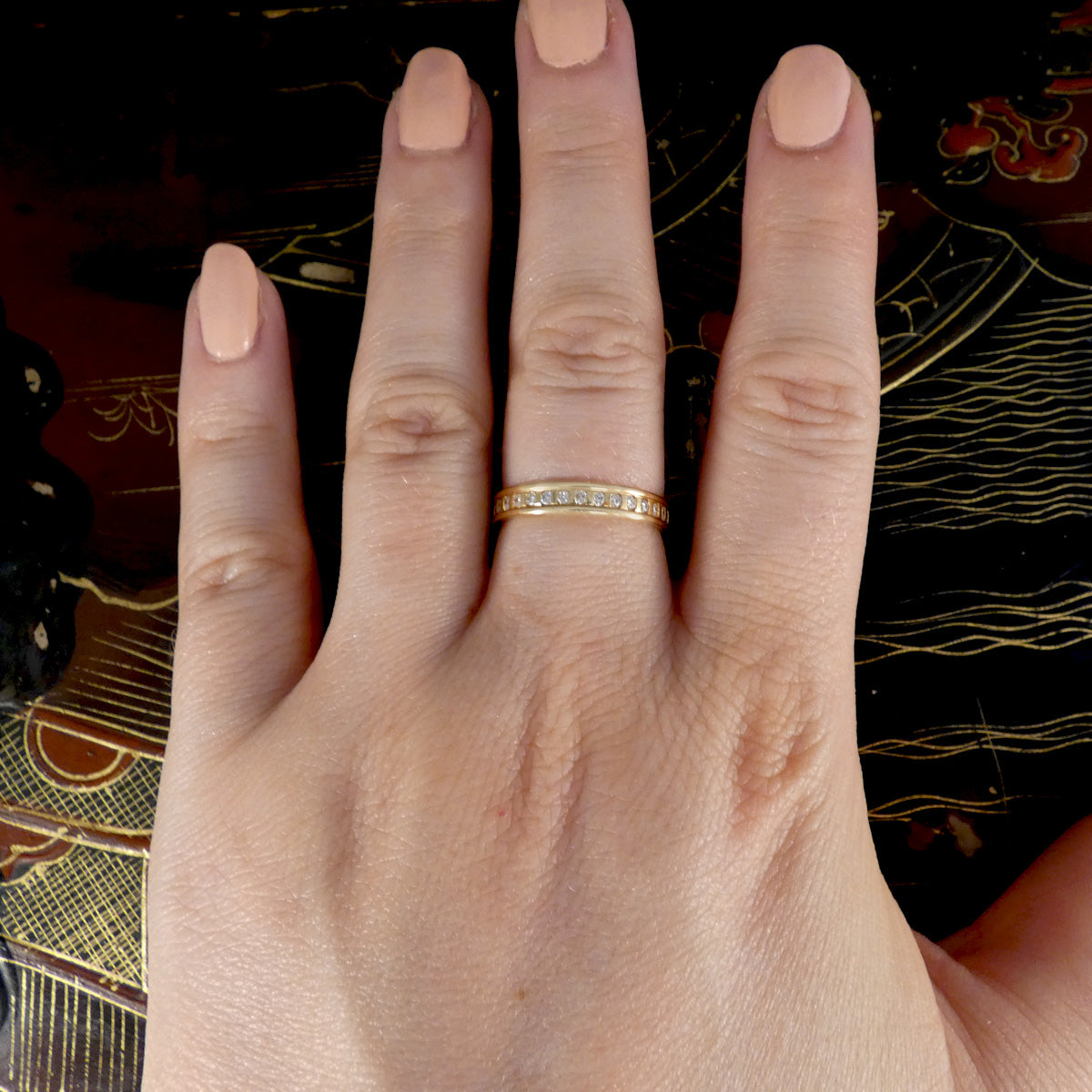 Hand wearing a gold and diamond full eternity ring with a decorative background
