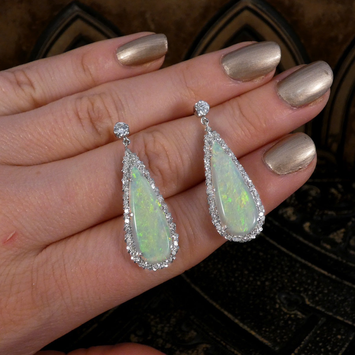Handheld view of vintage opal and diamond cluster drop earrings in platinum, highlighting the elegant teardrop opals with vibrant flashes of colour and a surrounding halo of brilliant diamonds.