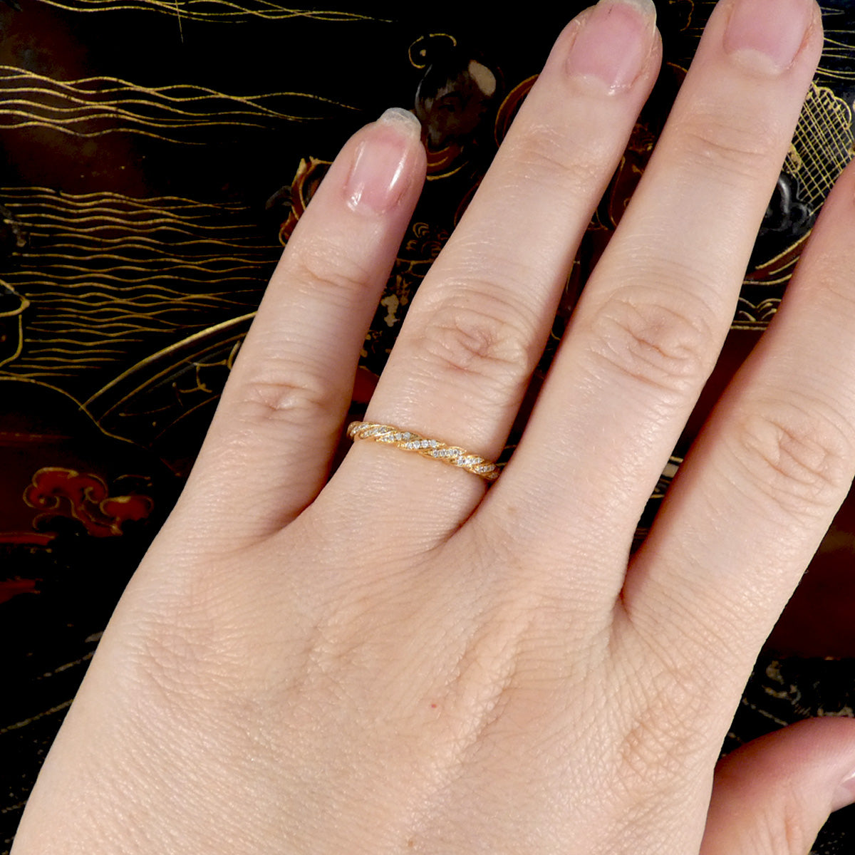 Hand wearing a gold ring with a decorative background
