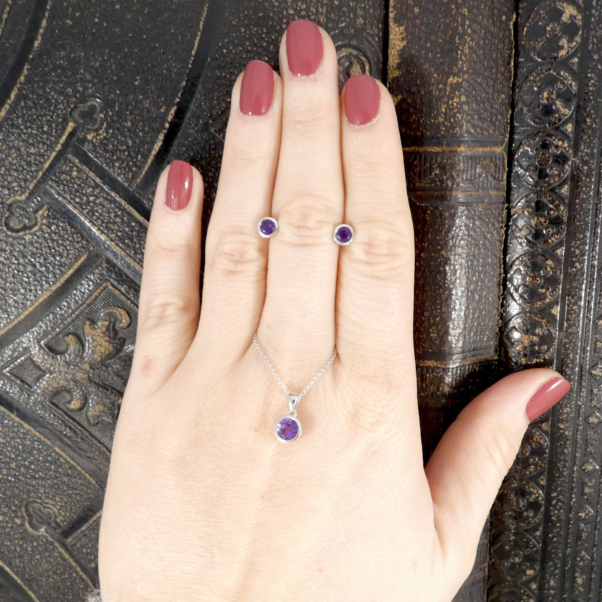 Hand wearing a silver ring with a purple gemstone against an ornate background