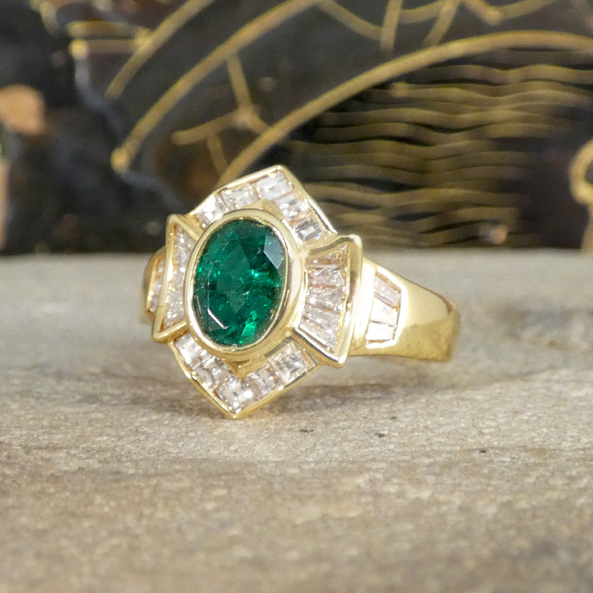 Elegant emerald and tapered diamond cluster ring set in yellow metal, testing as 18ct yellow gold, featuring a vivid oval emerald centre stone surrounded by shimmering tapered baguette diamonds.