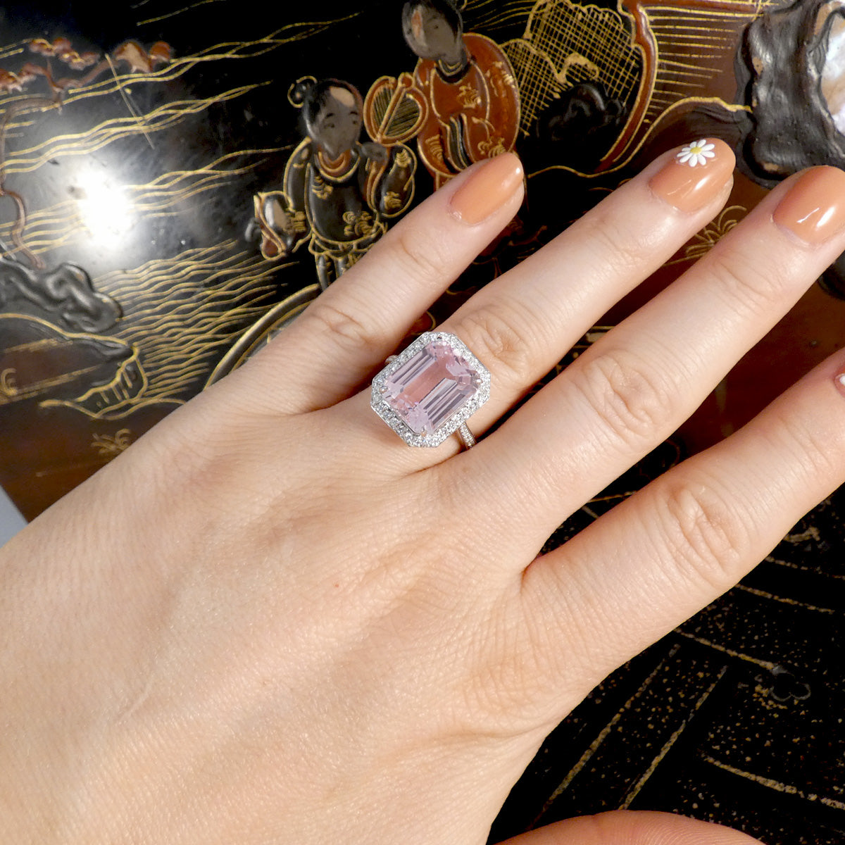 Hand wearing a pink gemstone ring with a decorative background