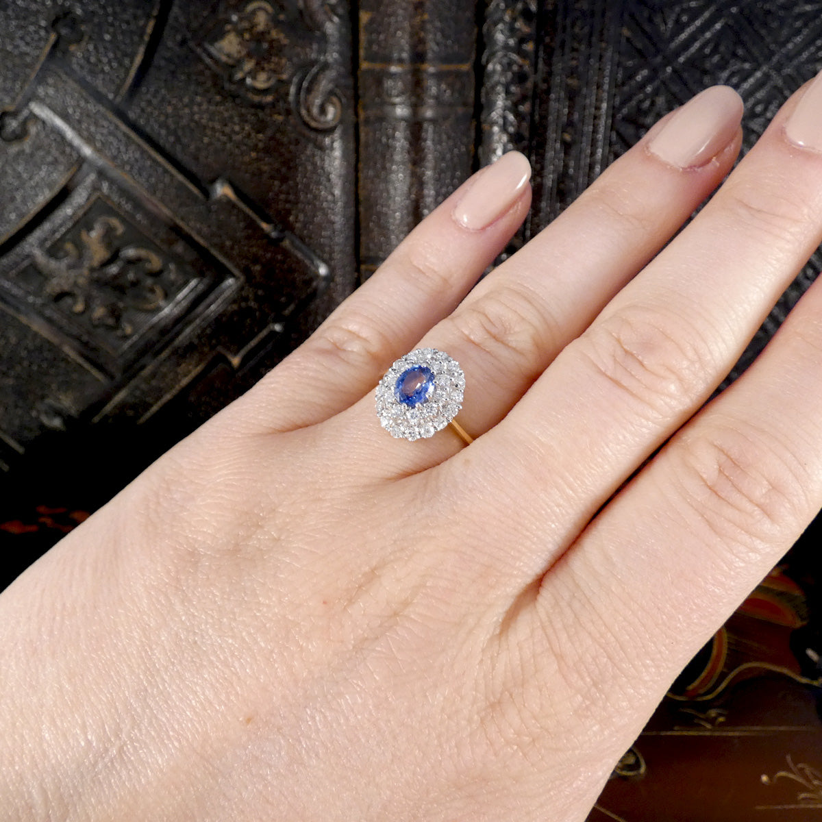 Elegant oval-cut blue sapphire and diamond cluster ring displayed on a hand, showcasing a white gold setting with a yellow gold band.