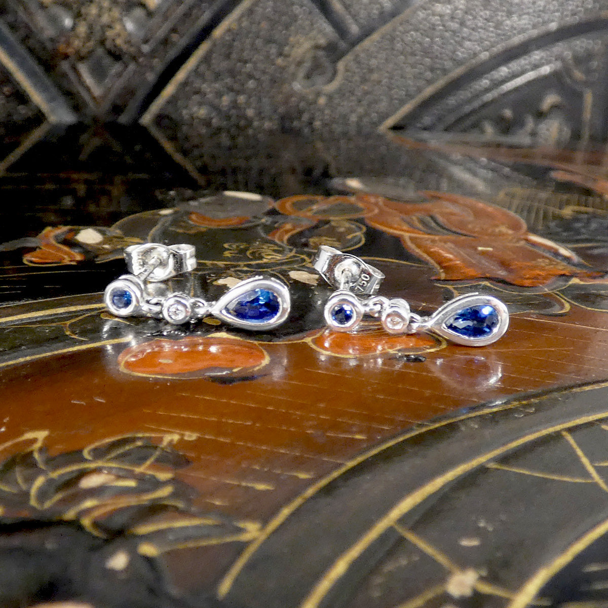 Pair of white gold earrings with blue gemstones on an ornate wooden surface
