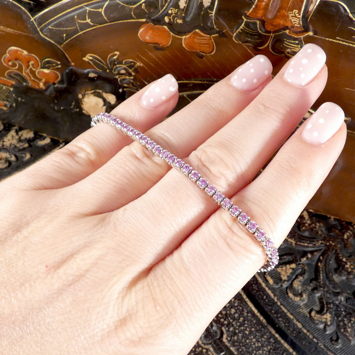 A pink sapphire and diamond tennis bracelet in white gold shown on the hand