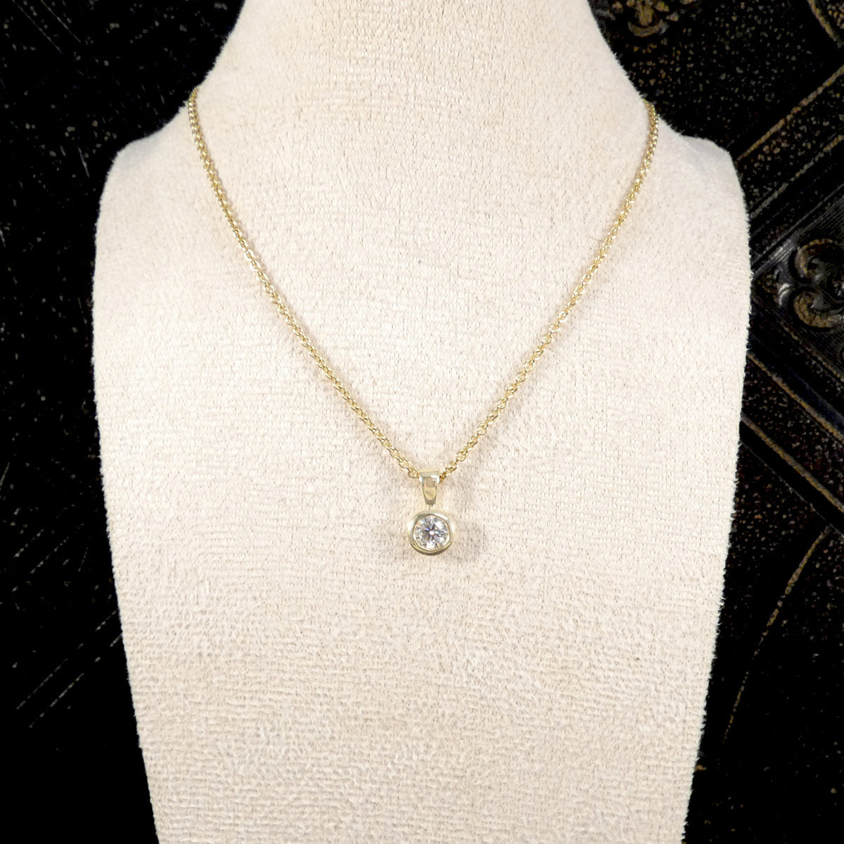 Gold necklace with a diamond pendant on a mannequin bust against a black background