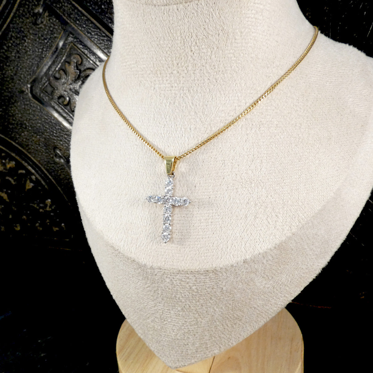 Diamond cross pendant necklace displayed on a cream velvet bust, showcasing its brilliance and two-tone 18ct yellow and white gold setting.