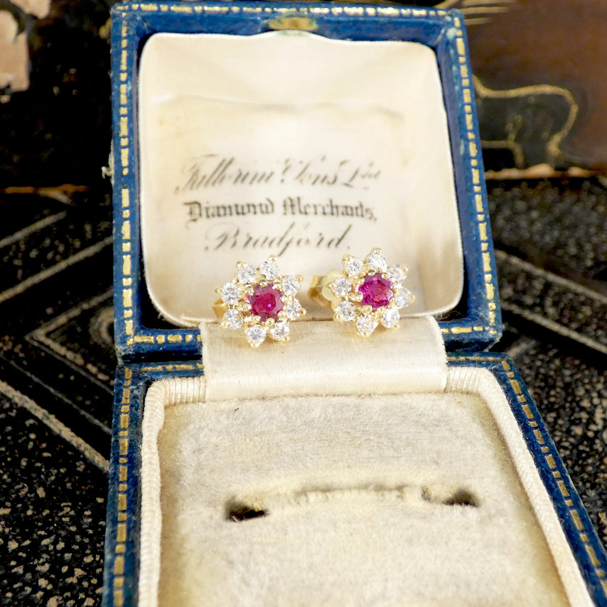 Pair of diamond and ruby earrings in an open jewelry box with visible branding.