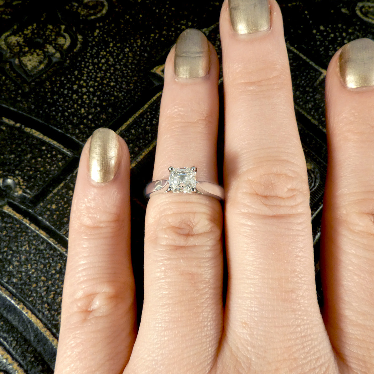 A Squared Emerald Cut Diamond Solitaire Engagement Ring in a four claw setting with a chunky Platinum band and modern feel. Shown on finger with small ring finger size and resizeable.