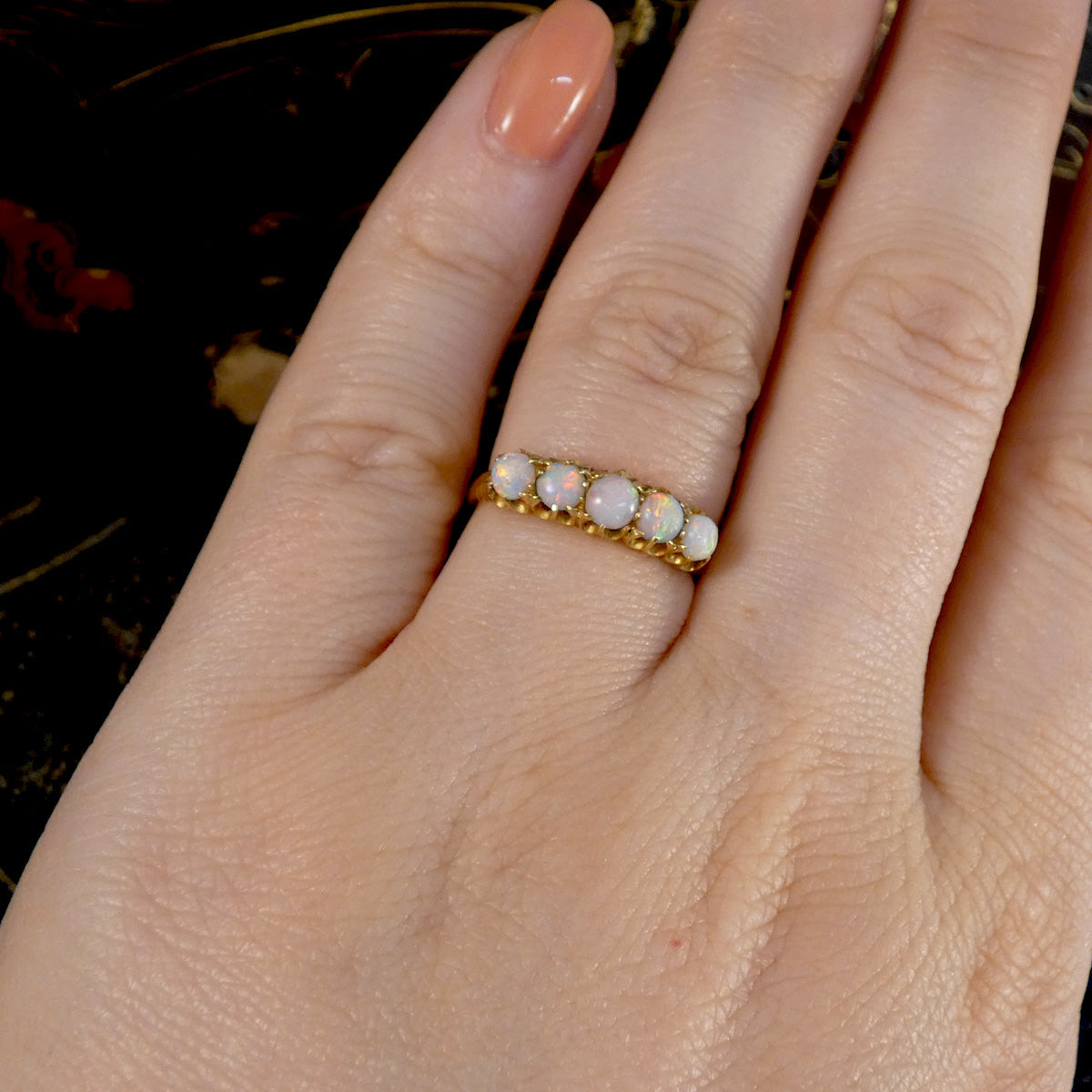 Gold ring with opal stones on a hand against a dark background