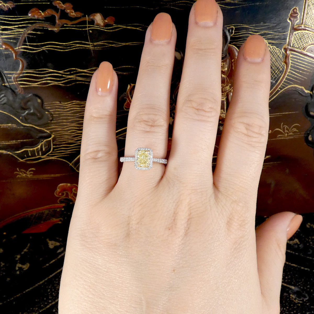 Hand wearing a yellow and white diamond ring with an ornate background