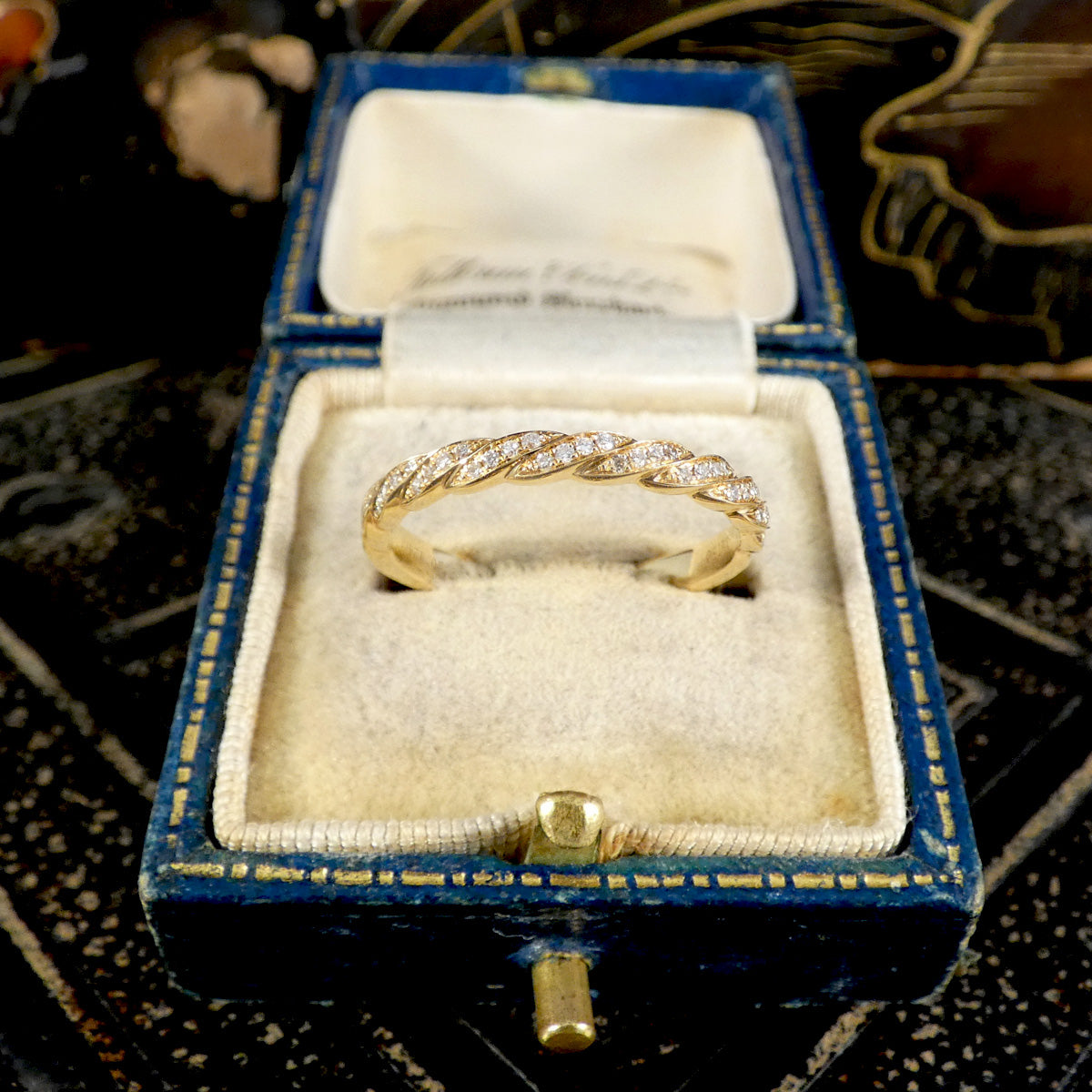 Gold ring with diamonds in a blue jewelry box on a patterned surface