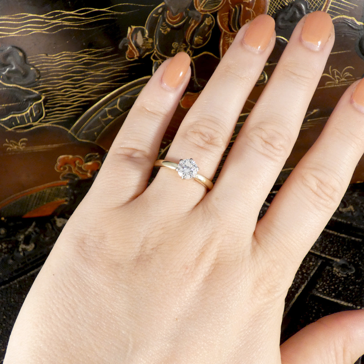 Hand wearing a gold ring with a diamond on an ornate background