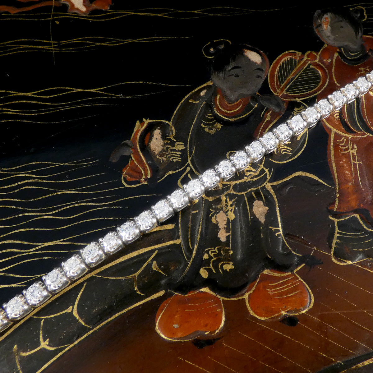 Diamond tennis bracelet showcasing a continuous row of round brilliant-cut diamonds set in white gold, with a vintage lacquered background.