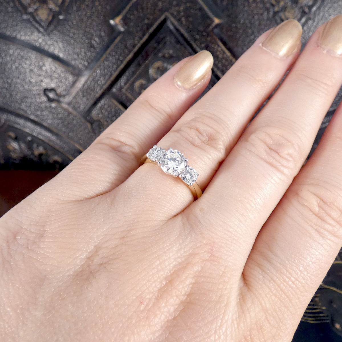 Hand wearing a diamond three stone ring with a textured background