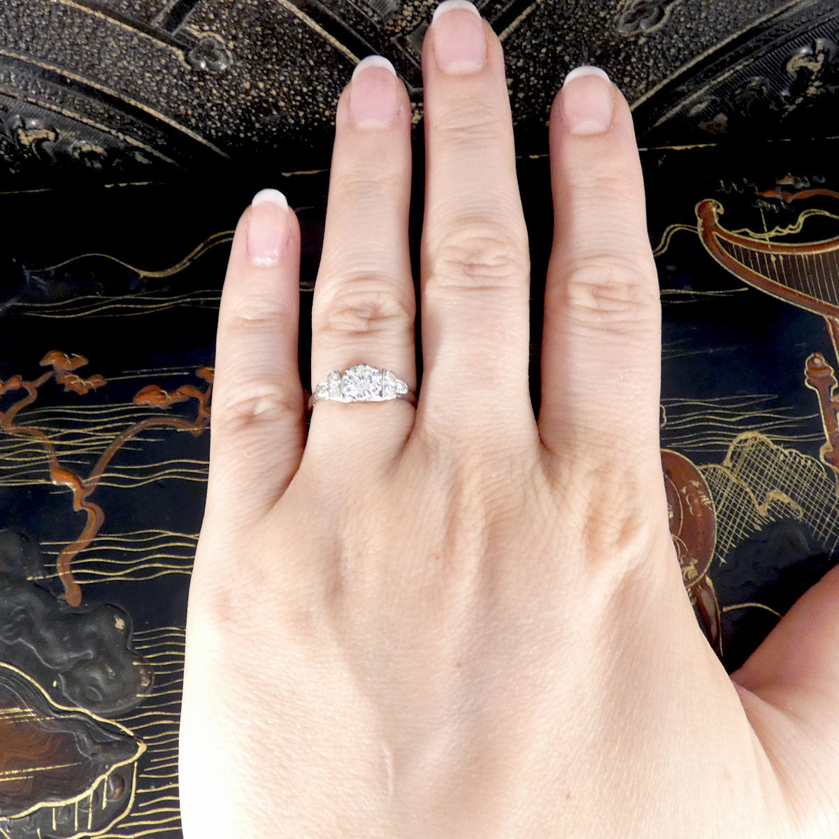 Hand wearing a diamond ring with an ornate background