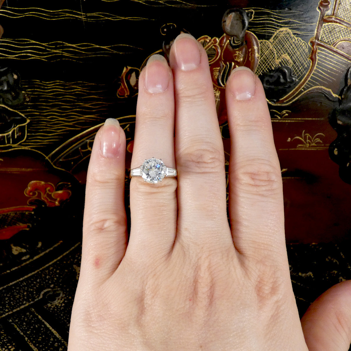 Hand wearing a diamond ring with an ornate background