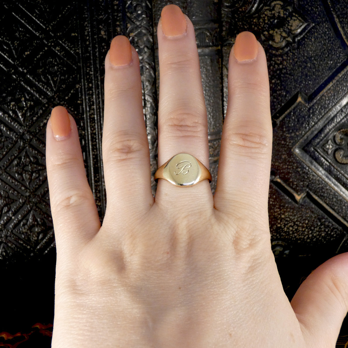 Hand wearing a gold signet ring with a visible 'B' on.